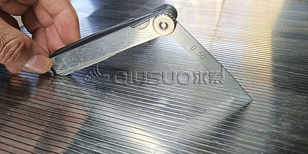 A hand is measuring slot size of the wedge wire screen panel with feeler gauge.